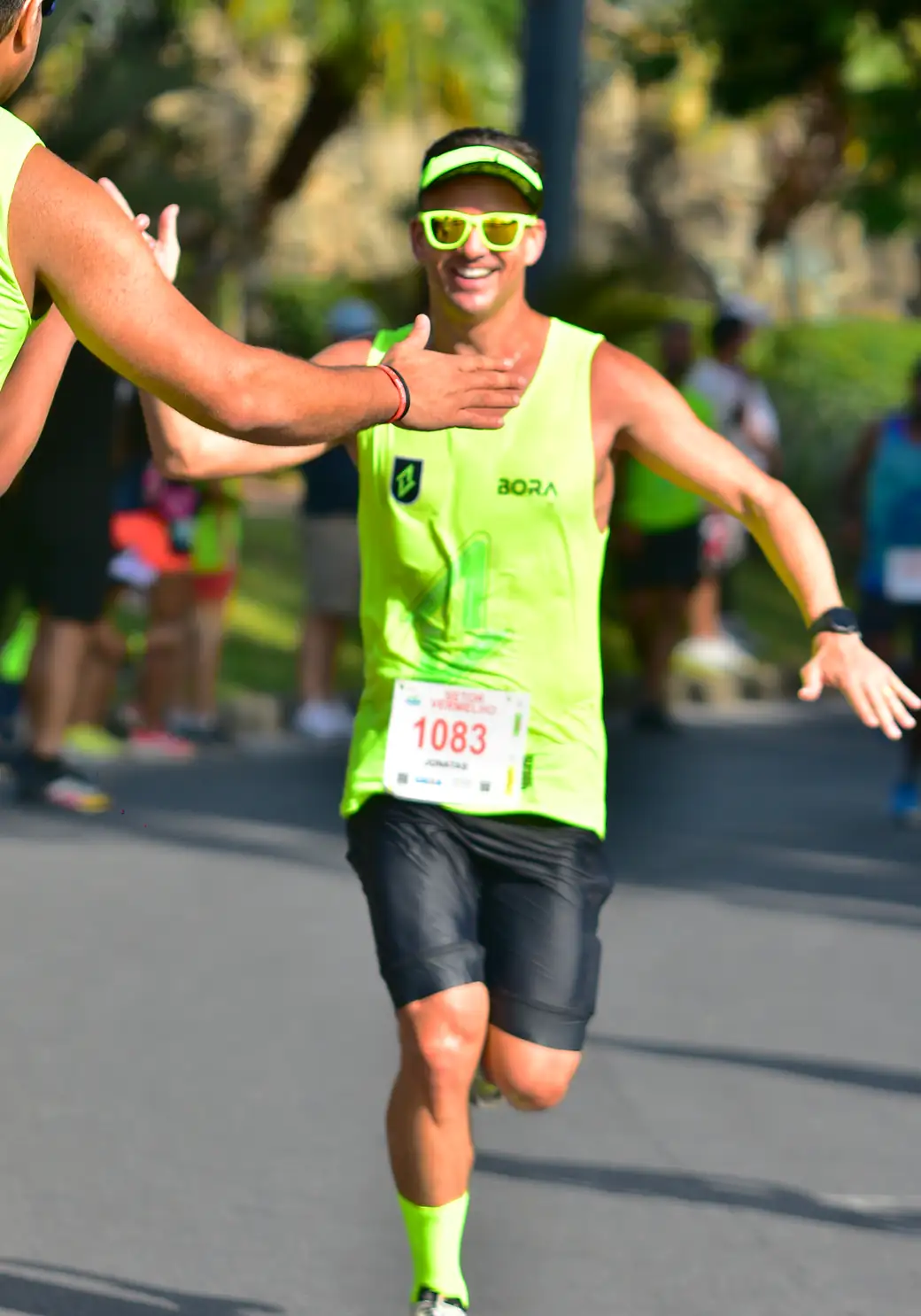 Atleta da BORA correndo de braços abertos, com o uniforme verde neon